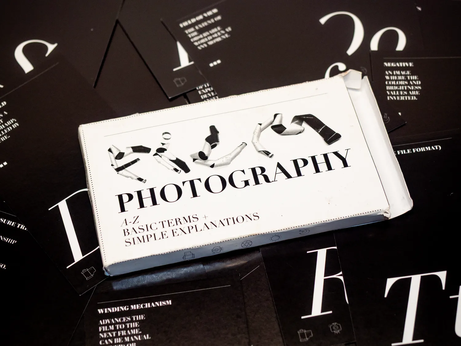 Close-up of a book titled 'Photography' with black and white cover design, placed on a dark surface with scattered papers.